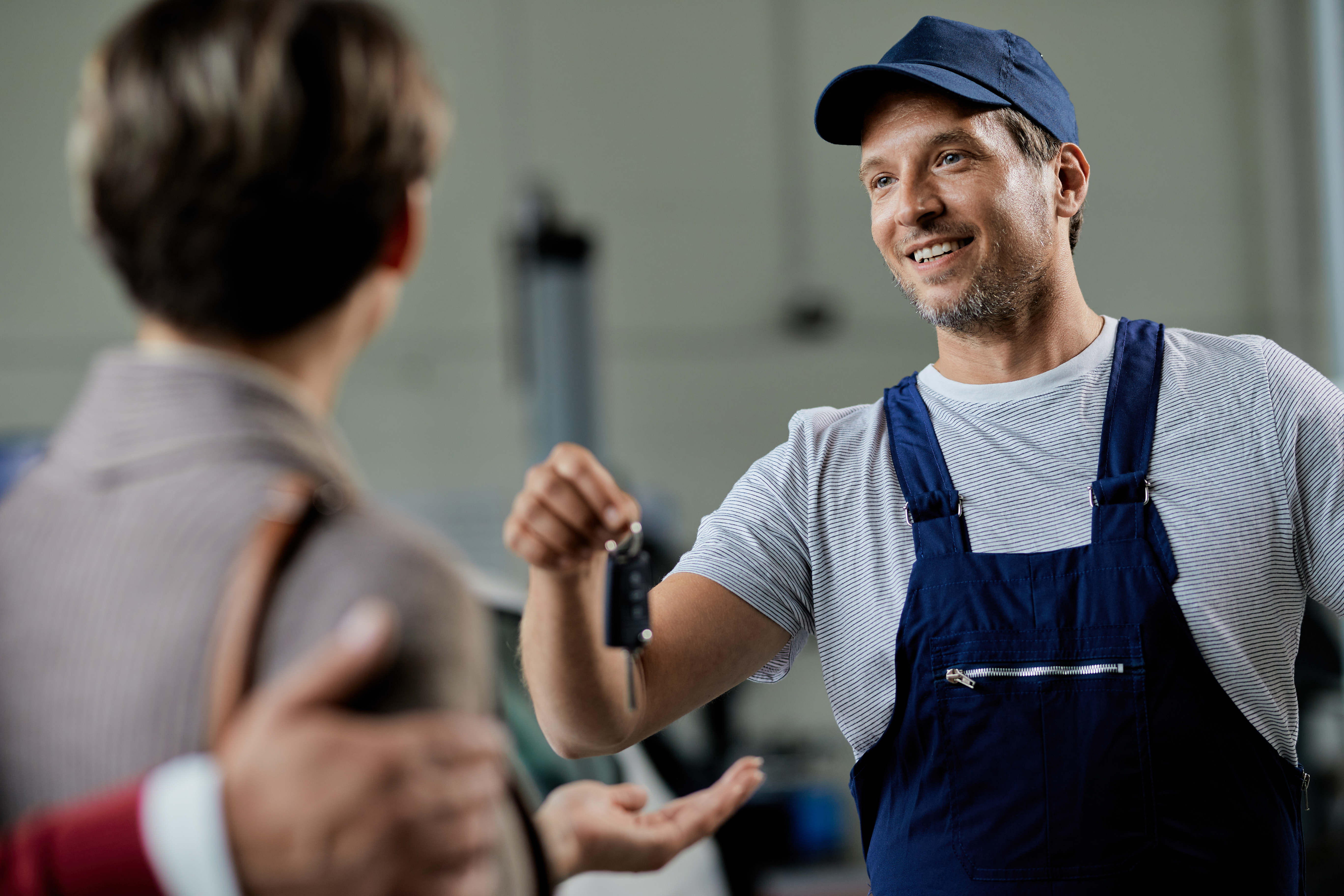 Happy mechanic giving car key to his customer in auto repair shop.